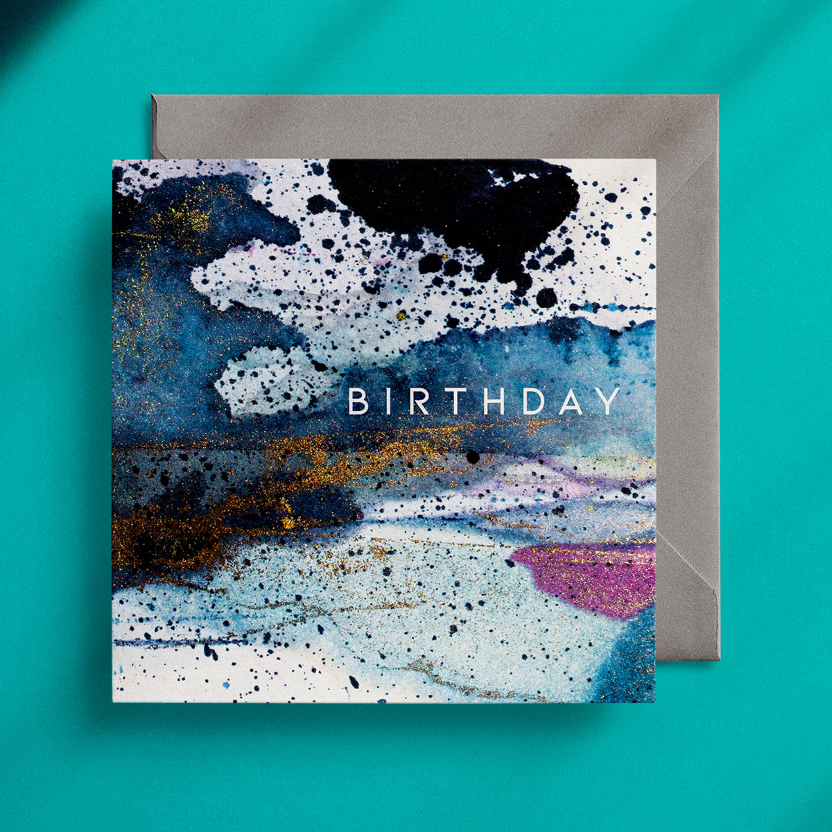 Dark blue, ink spattered, square birthday card with a grey envelope on a green background