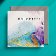 "Congrats!" square greeting card with a turquoise, gold and purple ink design on a grey envelope