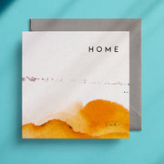 Orange and white design that looks like hills on a square greeting card which reads the word "Home" at the top