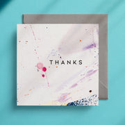 Square greeting card with the word "Thanks" in the centre with a minimalist, abstract design
