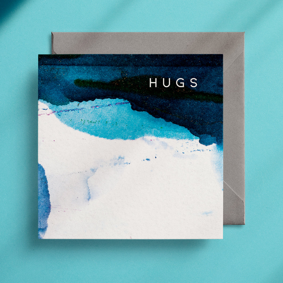 Blue and white square greeting card on turquoise background with the word "Hugs" written on it