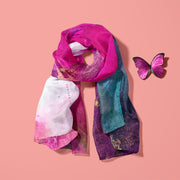 Bright pink, purple, white and gold luxurious silk twill scarf laid on a peach background with a pink butterfly next to it