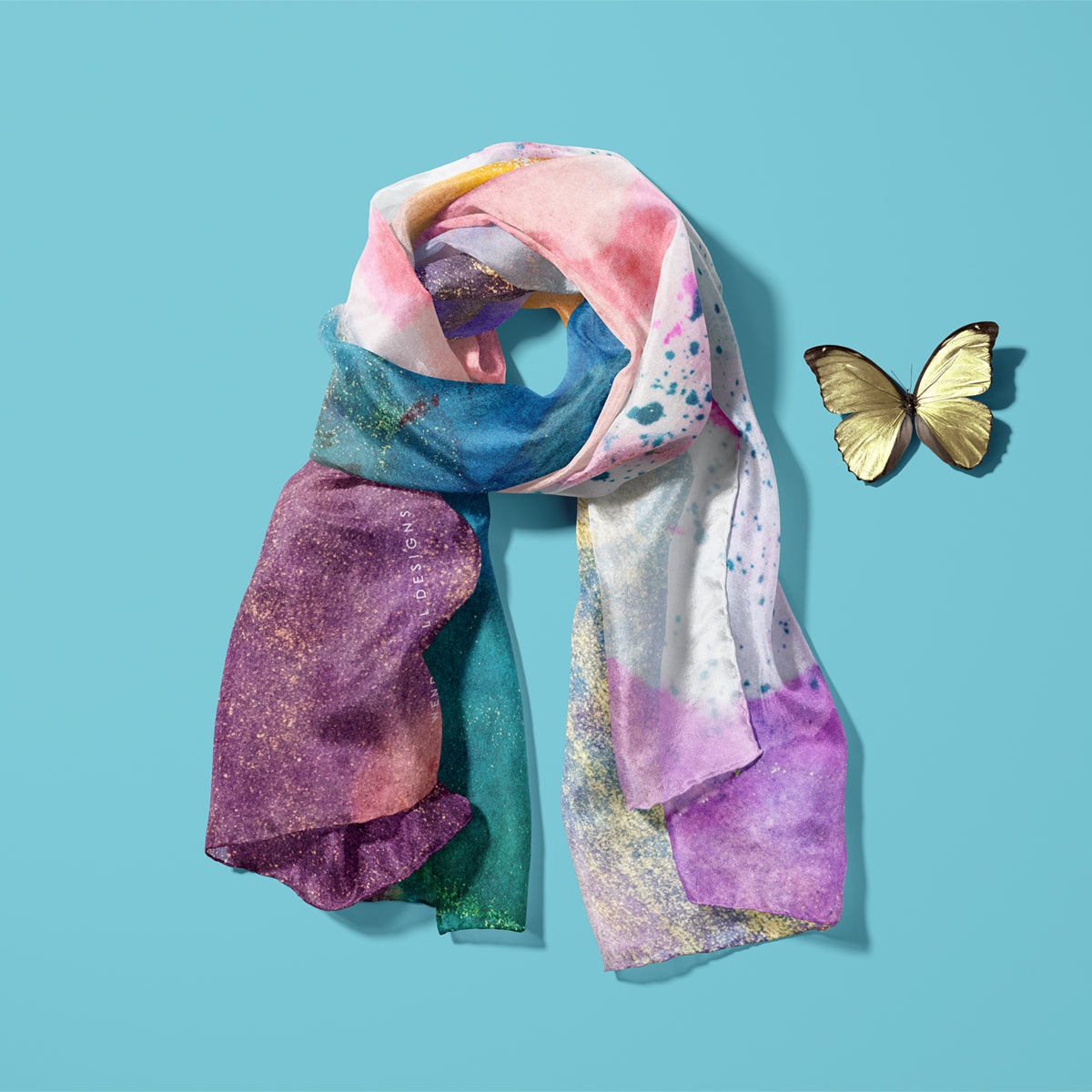 Light and soft, feminine silk scarf with a pretty pattern laid on a blue background with a yellow butterfly next to it