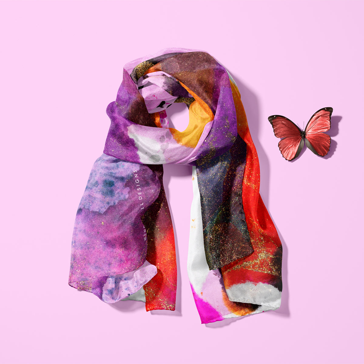 Fiery orange and purple, light silk twill scarf laid on a pink background with a red butterfly next to it